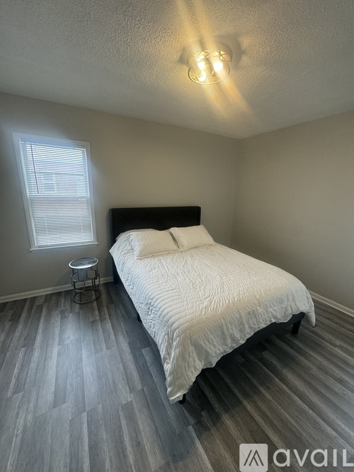 A bedroom with a bed, a small table, and a window with blinds.