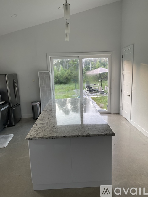 A kitchen with a marble countertop and a view of a backyard through a sliding glass door.