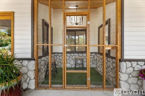 A wooden screen door with a mesh design is open, revealing a living room with a sofa and a coffee table.