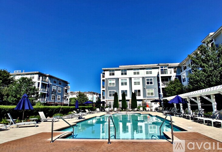 A swimming pool surrounded by lounge chairs and umbrellas in front of a multi-story apartment building.