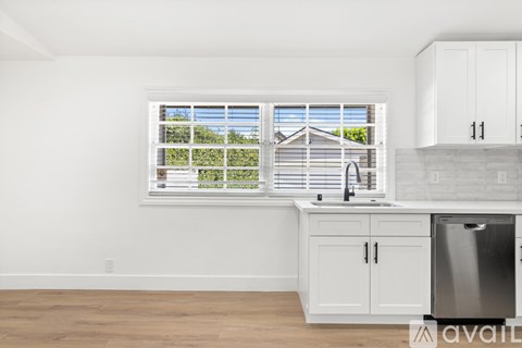 A kitchen with white cabinets and a window overlooking a house.