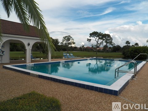A pool surrounded by a gravel area and a white arched building.