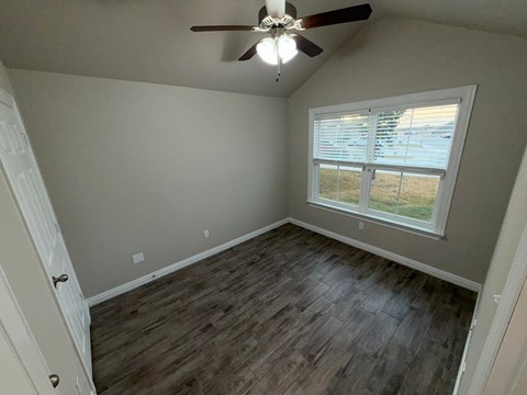 A room with a ceiling fan and a window overlooking a field.