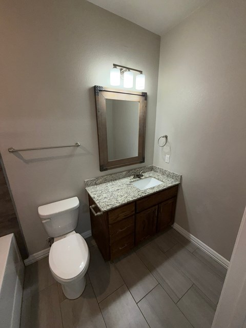 A bathroom with a toilet, sink, mirror, and wooden cabinets.