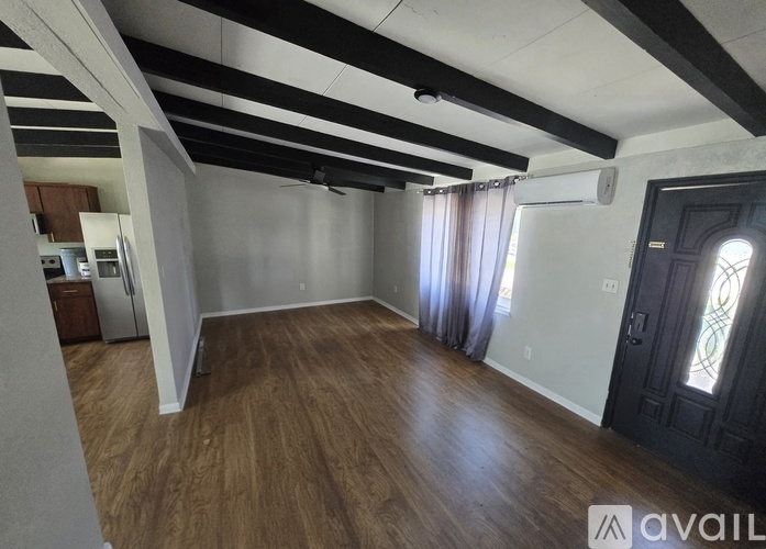 A spacious room with wooden flooring and a black door.