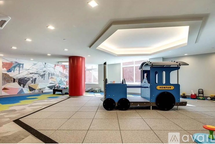 A blue Kompan toy truck is in a spacious room with a red column and a mural on the wall.