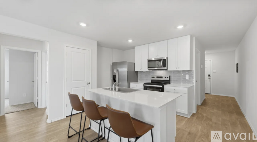 A kitchen with white cabinets and a white island with brown chairs.