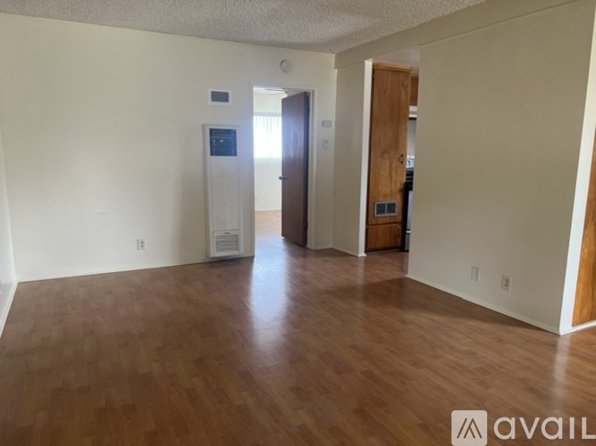 A room with wooden floors and white walls, with a door on the right and a wall-mounted device on the left.