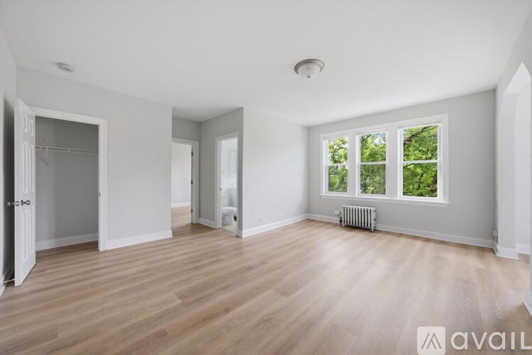 A spacious room with wooden flooring and a window showing greenery outside.