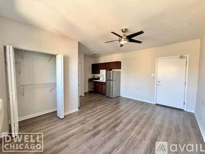 A spacious room with a ceiling fan and a kitchenette in the background.