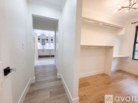 A room with wooden flooring and white walls, leading to a kitchen area.