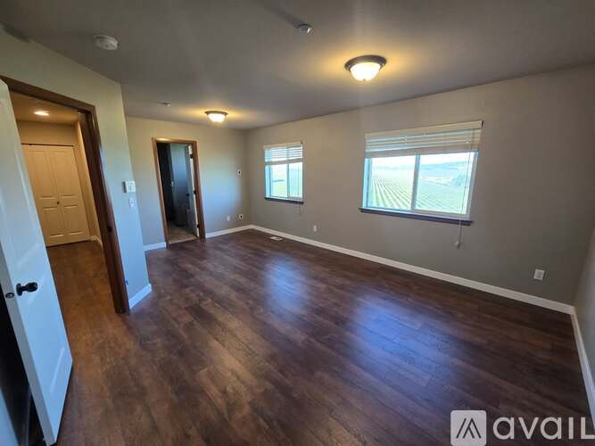 A spacious room with wooden floors and two windows.
