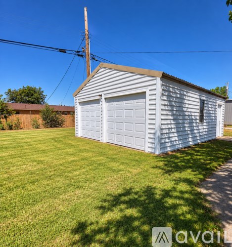 A small white garage with a corrugated metal roof is situated in a grassy area.