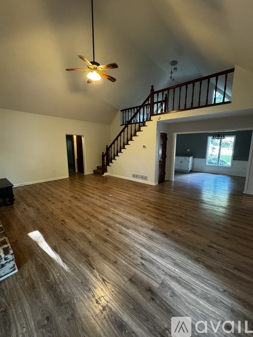 A spacious room with wooden flooring and a staircase.