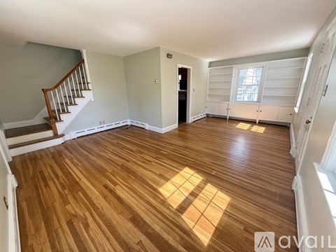 A spacious room with wooden flooring and a staircase on the left side.