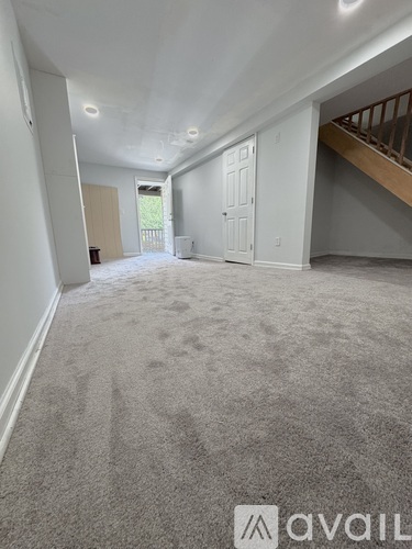 A spacious room with carpeted floor and a staircase on the right side.