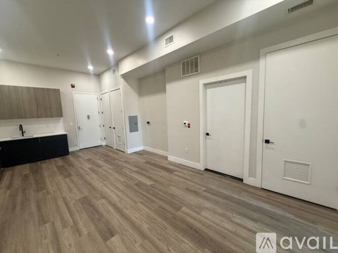 A room with wooden flooring and white walls, featuring a kitchen area with cabinets and a countertop.