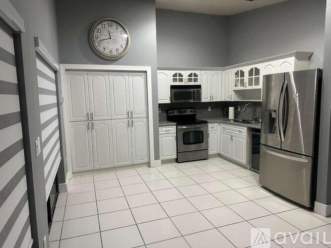 A kitchen with a clock on the wall and a refrigerator on the right.
