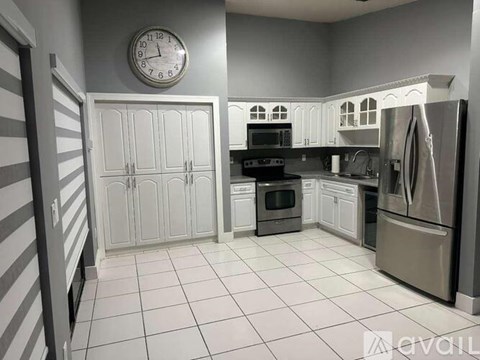A kitchen with a clock on the wall and a refrigerator on the right.
