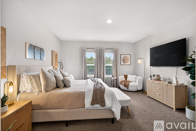 A well-lit bedroom with a large bed, a chair, and a TV.