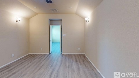 A room with wooden flooring and a door leading to another room.