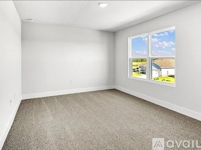 A room with a carpeted floor and a window showing a view of a house and trees.