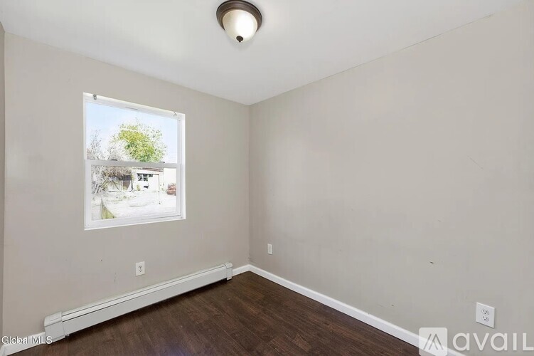 A room with a window showing a view of a street with houses and trees.