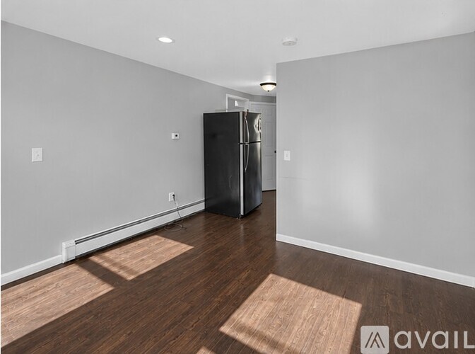 A room with a black fridge and wooden flooring.