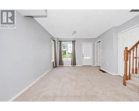 A spacious room with beige carpeting and white walls, with a staircase on the right side.