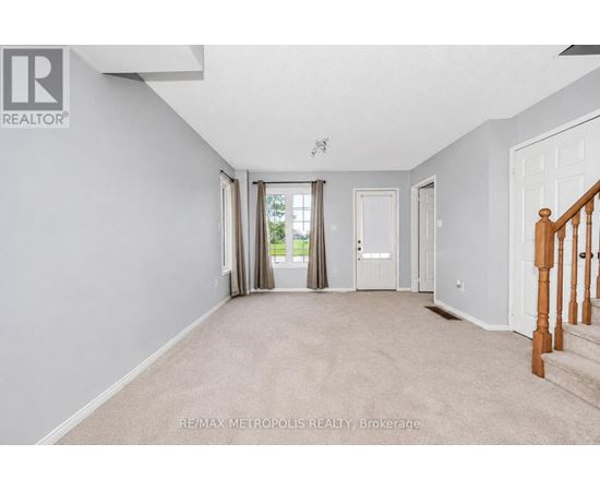 A spacious room with beige carpeting and white walls, with a staircase on the right side.