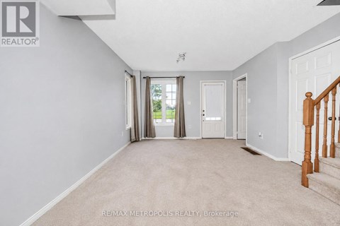A spacious room with beige carpeting and white walls, with a staircase on the right side.
