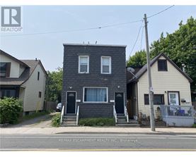 A two-story house with a grey brick exterior and a black door is for sale.