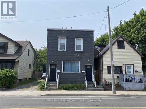 A two-story house with a grey brick exterior and a black door is for sale.