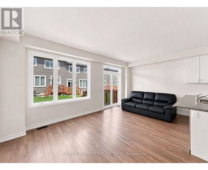 A living room with a black leather couch and a large window showing a view of a house.