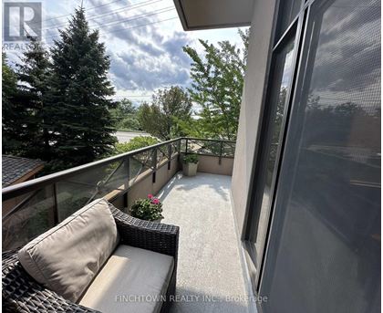 A balcony with a couch and a view of trees and a building.