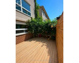 A wooden deck with a red chair and a tree in the middle.