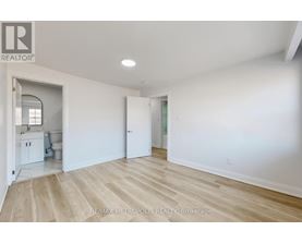 A spacious room with white walls and wooden flooring, with a doorway leading to another room.