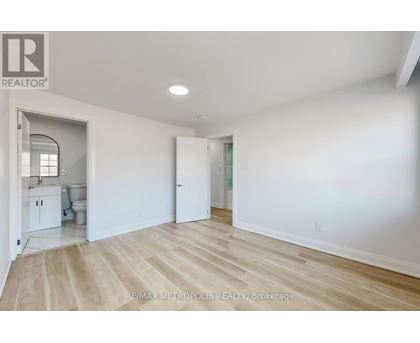 A spacious room with white walls and wooden flooring, with a doorway leading to another room.