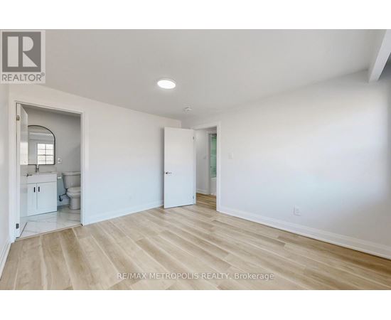 A spacious room with white walls and wooden flooring, with a doorway leading to another room.