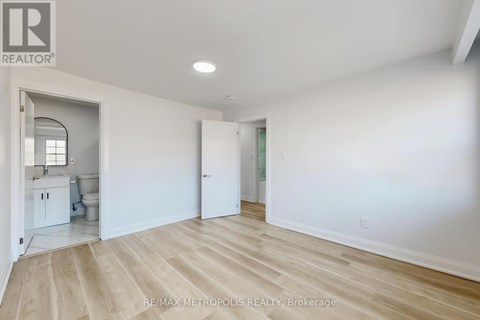 A spacious room with white walls and wooden flooring, with a doorway leading to another room.