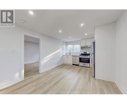 A spacious, empty room with a kitchenette in the background.