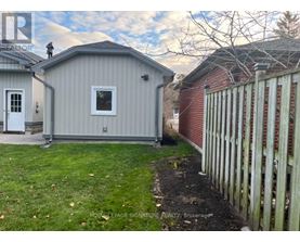 A grey shed sits next to a red brick building with a white picket fence in front.