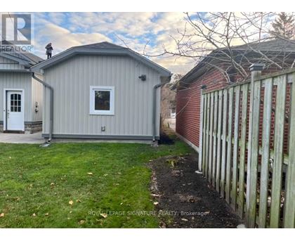A grey shed sits next to a red brick building with a white picket fence in front.