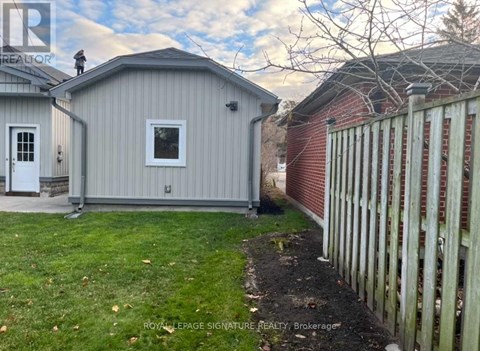 A grey shed sits next to a red brick building with a white picket fence in front.
