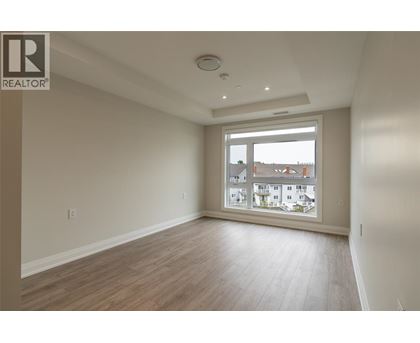 A spacious room with wooden flooring and a large window overlooking a residential area.