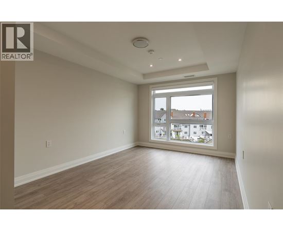 A spacious room with wooden flooring and a large window overlooking a residential area.