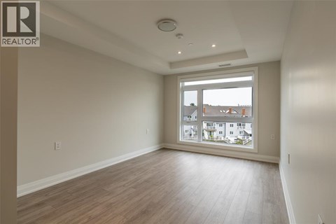 A spacious room with wooden flooring and a large window overlooking a residential area.