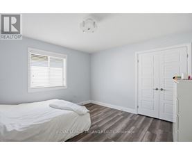 A bedroom with a bed, a window with blinds, a wooden floor, a white door, and a white dresser.