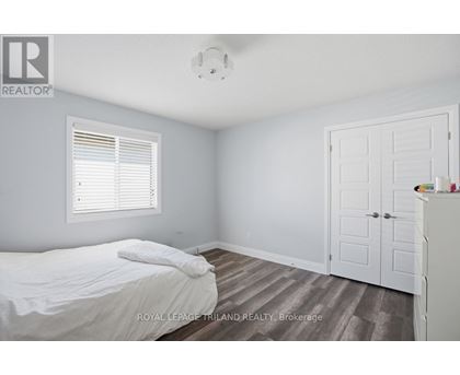 A bedroom with a bed, a window with blinds, a wooden floor, a white door, and a white dresser.