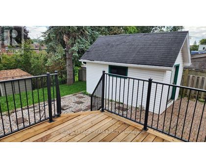 A small white building with a black roof and a green door is surrounded by a black metal fence.
